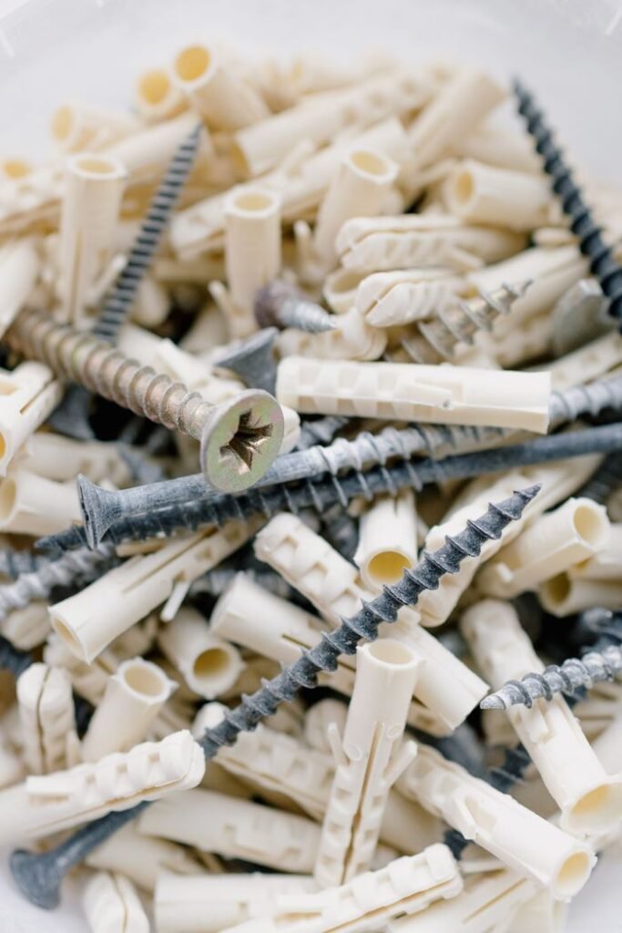 From above collection of metal screws and white plastic dowels heaped together in light room